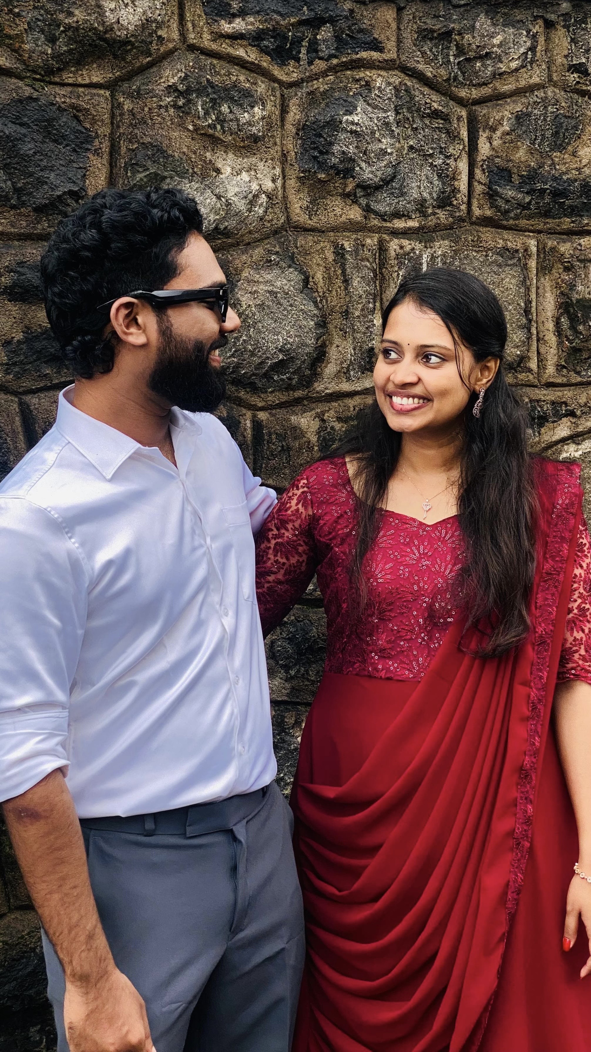 Jithin and Binju smiling beside a stone wall